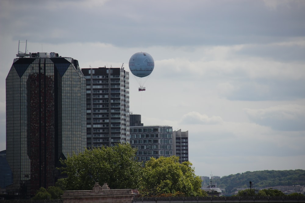 white and blue hot air balloon over green trees and high rise buildings during daytime