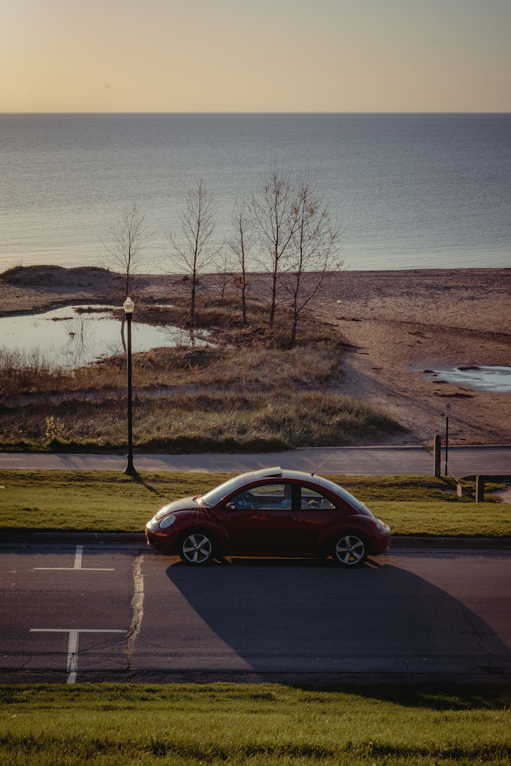 red sedan on road near body of water during daytime