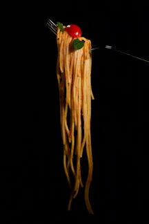 Close-up of perfectly cooked spaghetti twirled on a fork with fresh basil and cherry tomatoes.