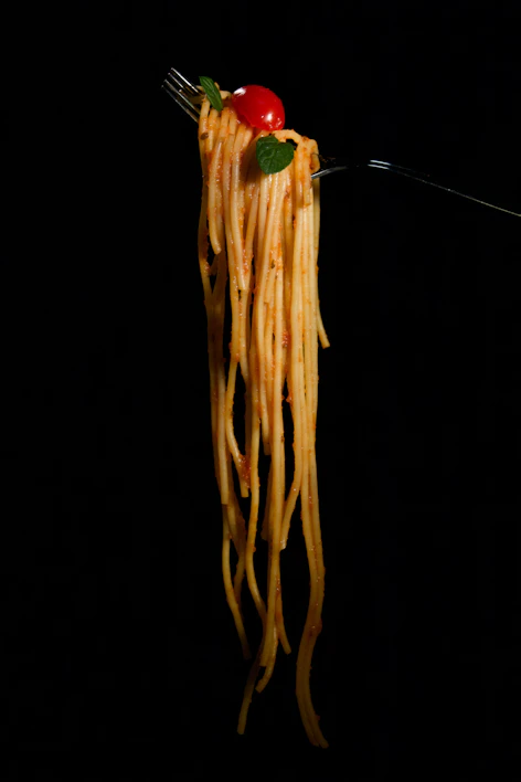 Close-up of perfectly cooked spaghetti twirled on a fork with fresh basil and cherry tomatoes.