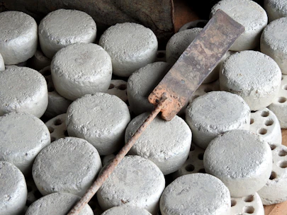 Numerous round, gray concrete discs are arranged closely together, with a rusty metal tool lying on top. The tool appears to be a flat, rectangular blade attached to a long handle.