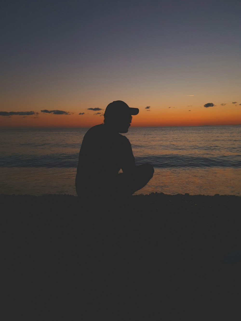 silhouette of man sitting on beach during sunset