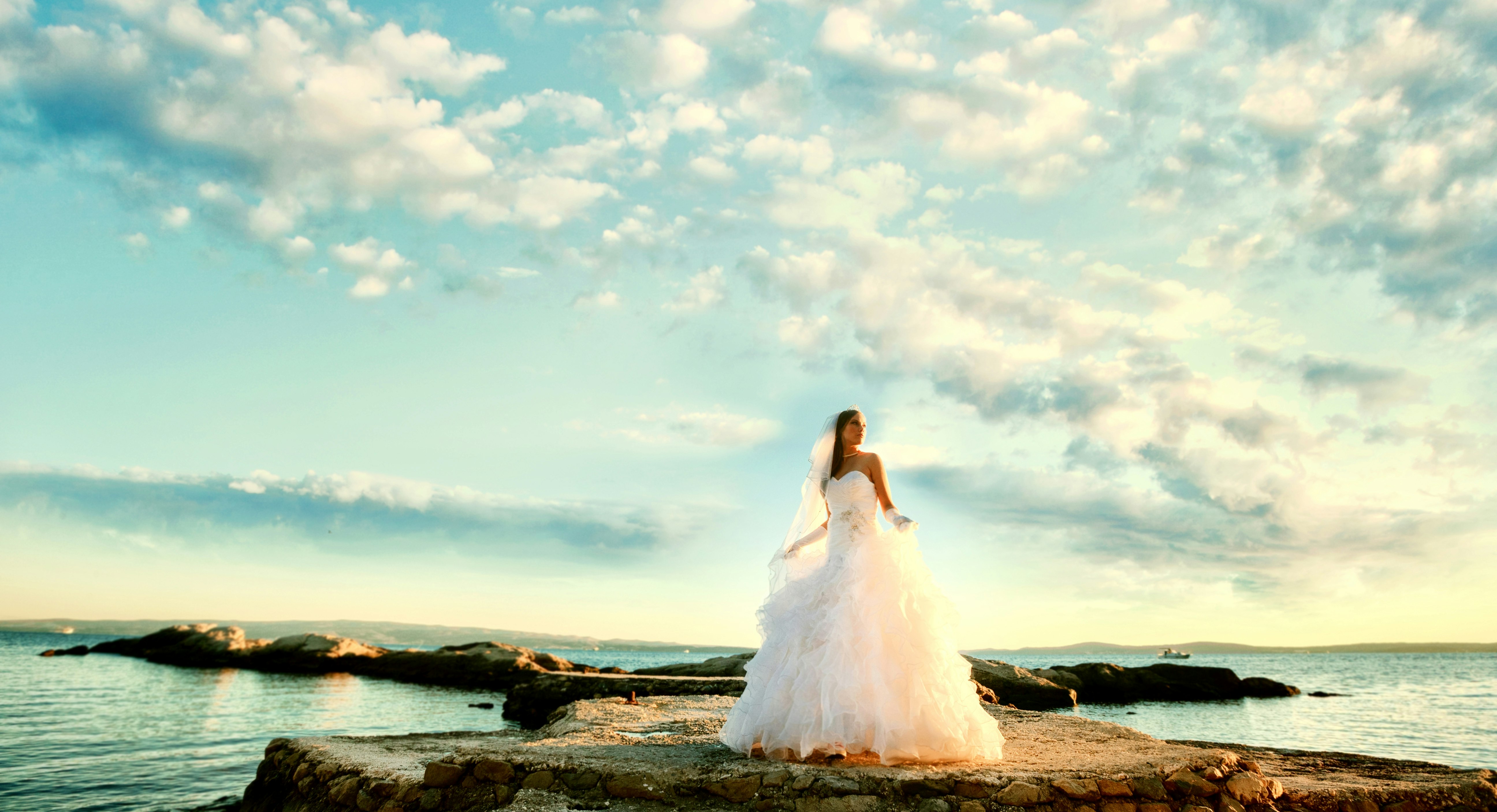 woman in white wedding dress standing on rock formation near body of water during daytime