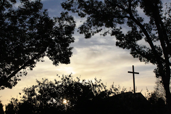 A serene sunset behind a wooden cross in a peaceful forest clearing.