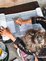 An artisan sketching a rug design on paper beside samples of yarn and fabric.