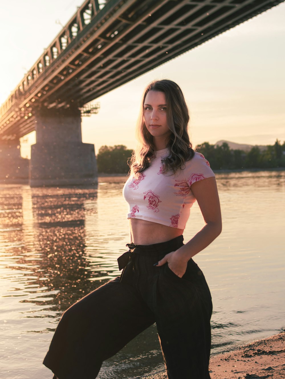 woman in pink t-shirt and black pants sitting on rock near body of water during