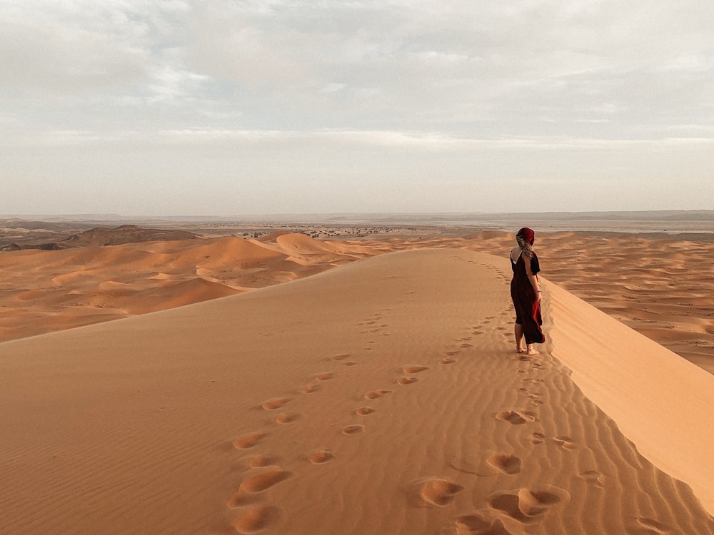 man in black jacket walking on desert during daytime