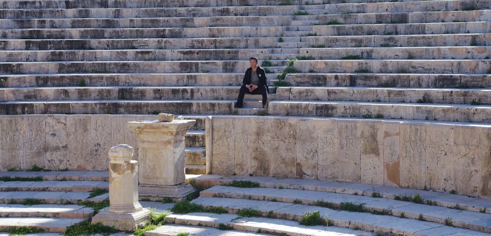 woman in black jacket and black pants sitting on gray concrete stairs