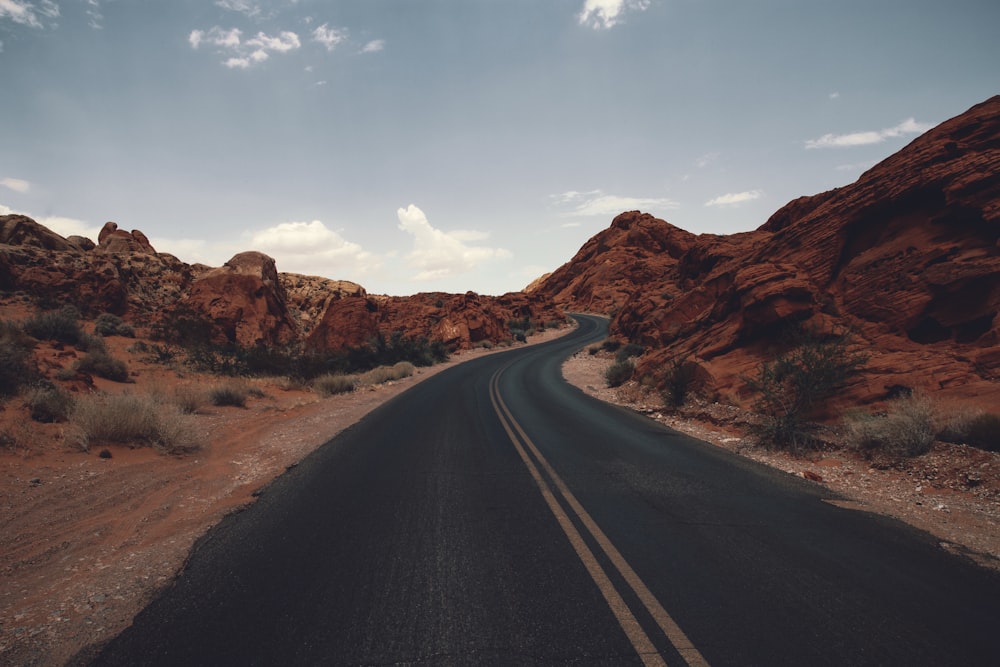 black asphalt road between brown rock formation under blue sky during daytime