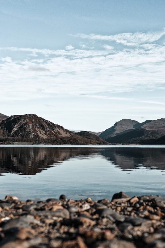 brown rocks on water near brown mountains under blue sky during daytime in Ennerdale Water United Kingdom