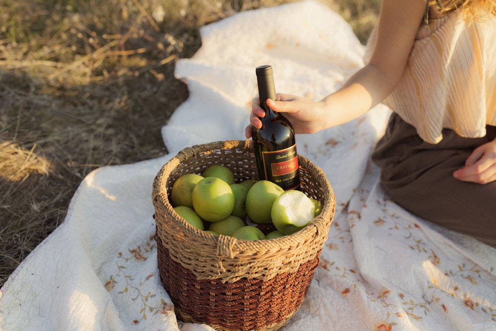 person holding brown wicker basket with green apples