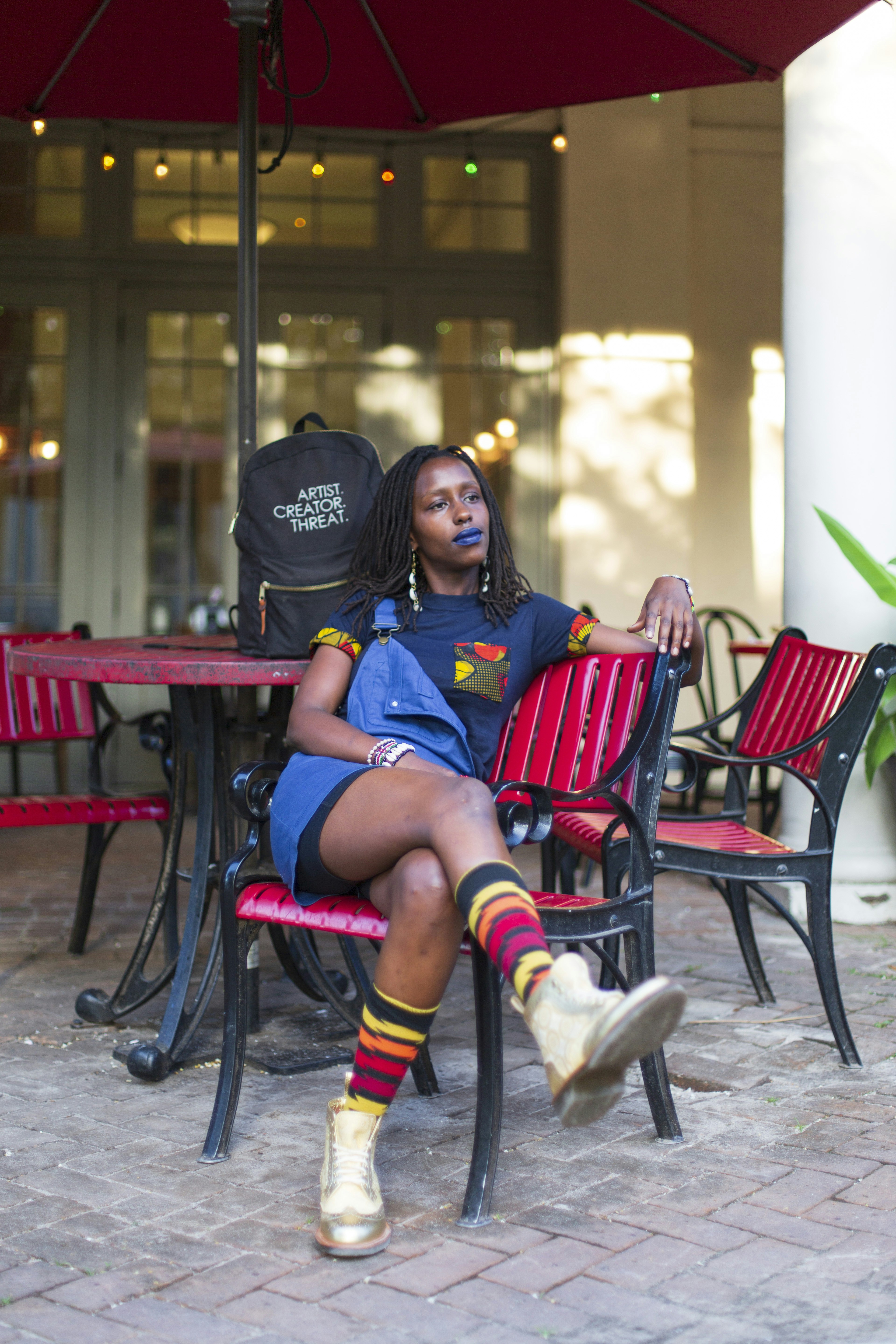 FreeQuency, an artist and community leader based out of New Orleans sitting on a red chair rocking her dreadlocked natural hair as part of This is Good Hair Project.
