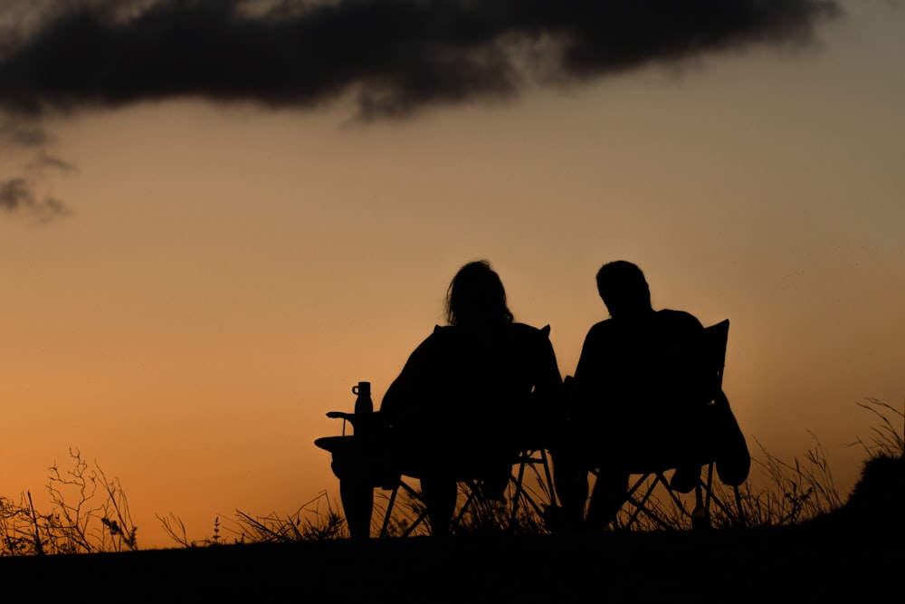 silhouette of 2 person sitting on bench during sunset