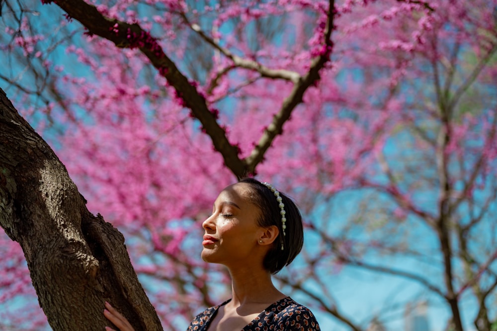 woman in black and white floral shirt standing beside pink cherry blossom tree during daytime