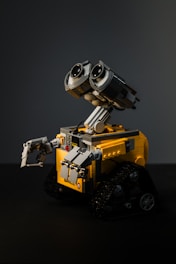 A LEGO model of a robot with large expressive eyes, featuring intricate details and movable parts. It has a yellow and gray color scheme with tank-like tracks for movement.