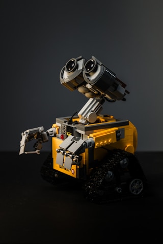 A LEGO model of a robot with large expressive eyes, featuring intricate details and movable parts. It has a yellow and gray color scheme with tank-like tracks for movement.