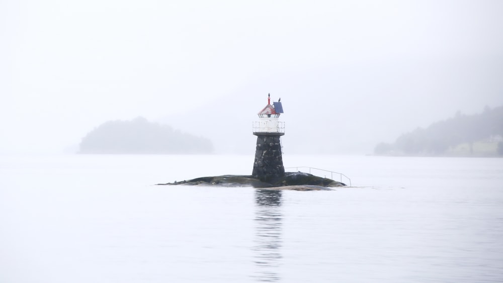 white and black lighthouse on black rock surrounded by water