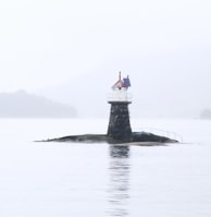 white and black lighthouse on black rock surrounded by water