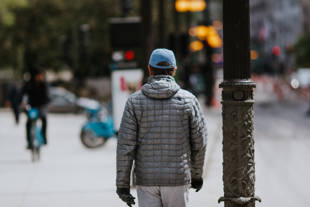 man in grey jacket wearing black helmet standing near black post during daytime