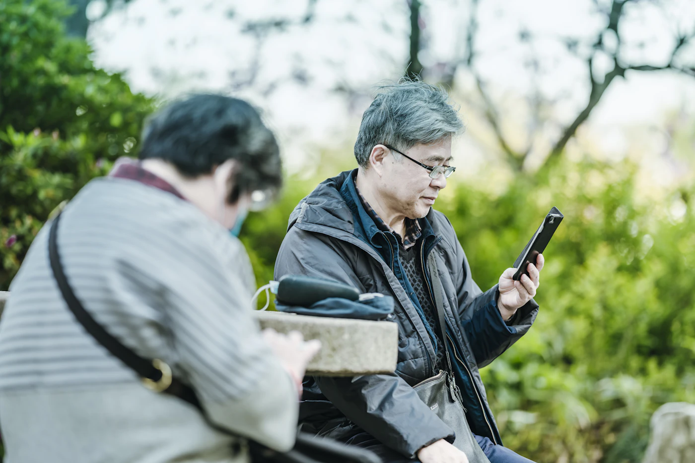An older man reading his phone outdoors beside a companion
