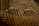 A pair of oval-shaped eyeglasses with thin metal frames is resting on a textured, patterned fabric. The fabric has alternating diagonal stripes in warm earth tones, creating a cozy and vintage feel.