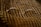 A pair of oval-shaped eyeglasses with thin metal frames is resting on a textured, patterned fabric. The fabric has alternating diagonal stripes in warm earth tones, creating a cozy and vintage feel.