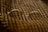 A pair of oval-shaped eyeglasses with thin metal frames is resting on a textured, patterned fabric. The fabric has alternating diagonal stripes in warm earth tones, creating a cozy and vintage feel.