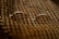 A pair of oval-shaped eyeglasses with thin metal frames is resting on a textured, patterned fabric. The fabric has alternating diagonal stripes in warm earth tones, creating a cozy and vintage feel.