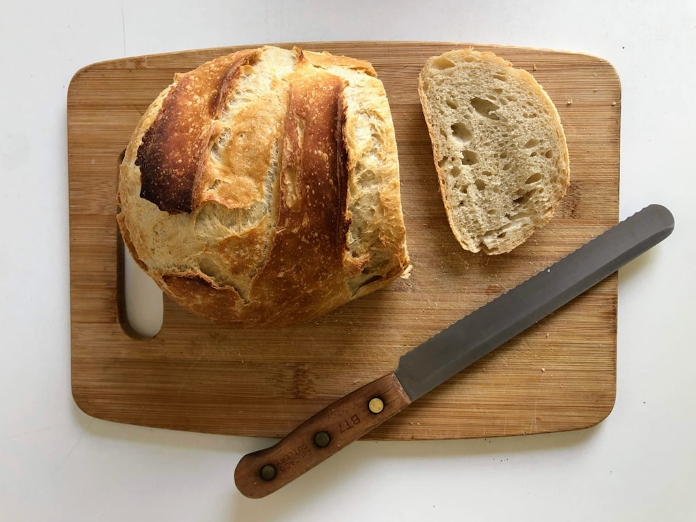 bread on brown wooden chopping board beside silver knife