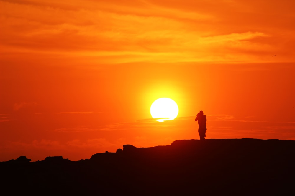 silhueta do homem de pé na montanha durante o pôr do sol