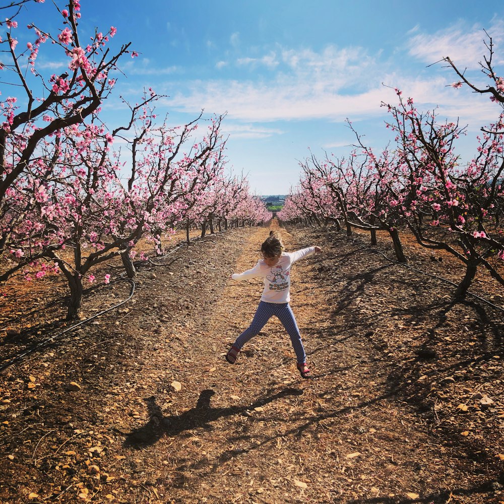 girl in white long sleeve shirt and black pants standing on brown field under blue and