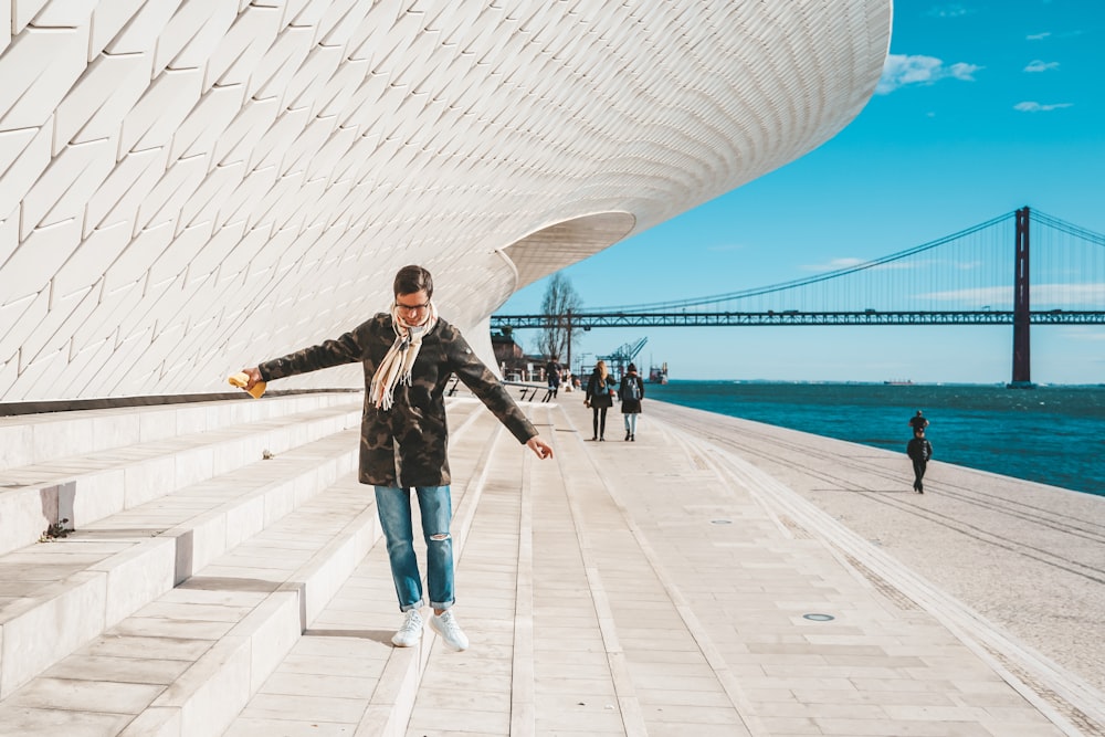 woman in black jacket and blue denim jeans standing on white concrete floor during daytime