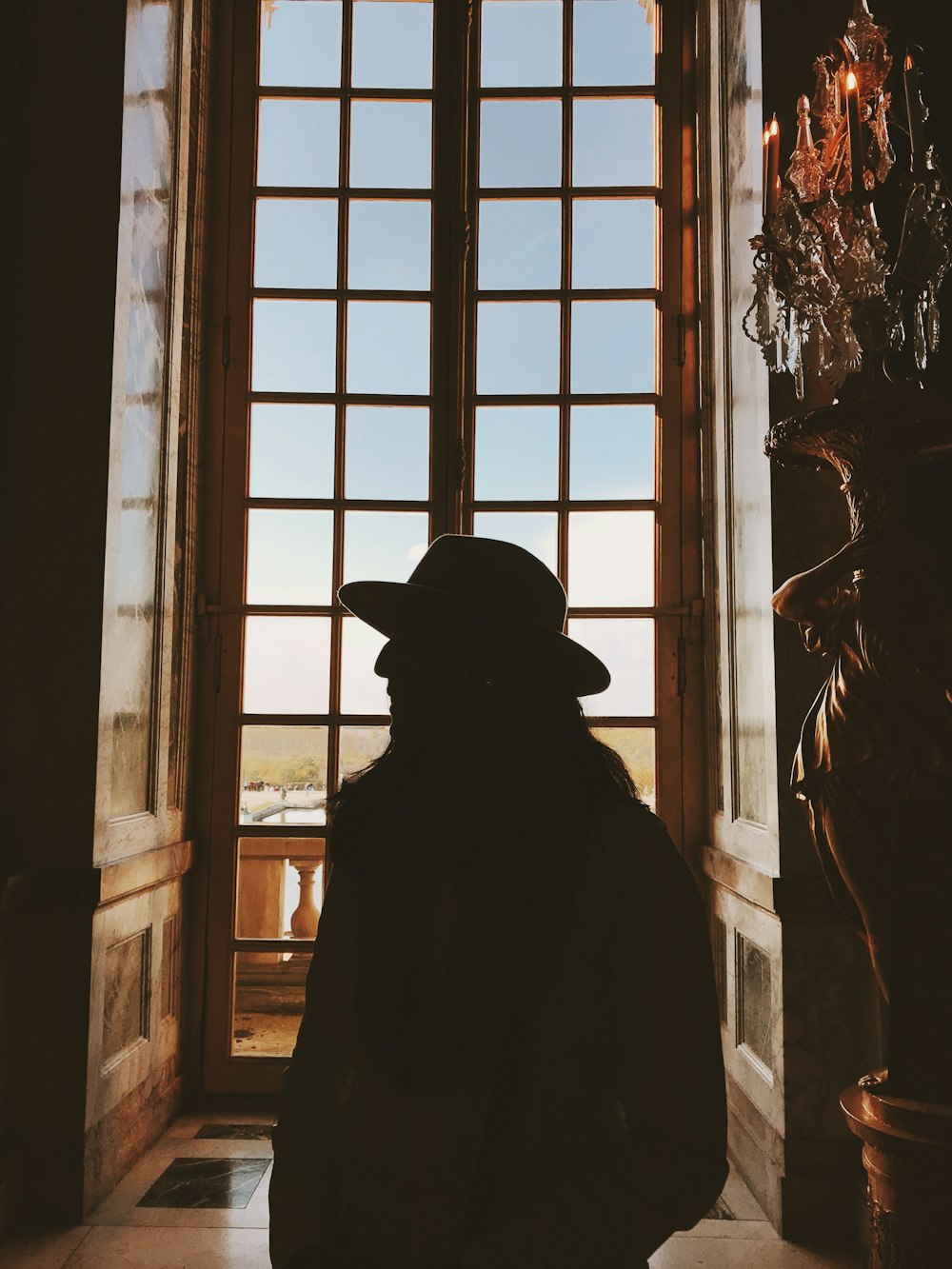 silhouette of person wearing hat and coat standing near window