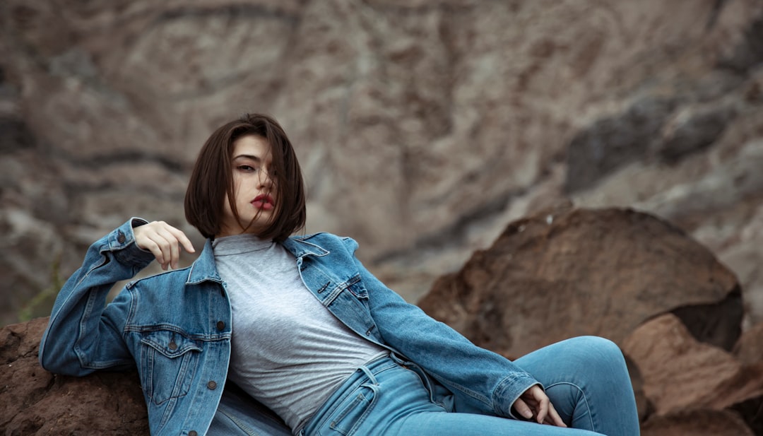 woman in blue denim jacket and blue denim jeans sitting on brown rock