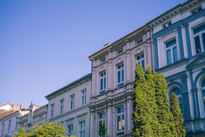 white concrete building with green trees in front under blue sky during daytime art noveau teams background