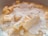 Chunks of butter are coated with a layer of fine white powdered sugar, mixing with a creamy liquid in a close-up view, suggesting the early stages of a baking preparation.