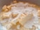 Chunks of butter are coated with a layer of fine white powdered sugar, mixing with a creamy liquid in a close-up view, suggesting the early stages of a baking preparation.