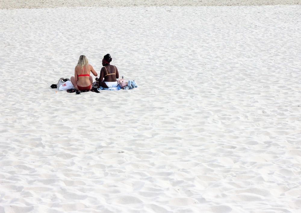 2 Frauen sitzen tagsüber auf Strandsand