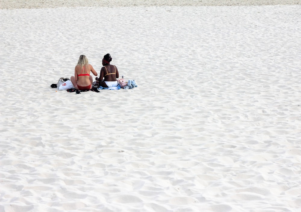 2 women sitting on beach sand during daytime