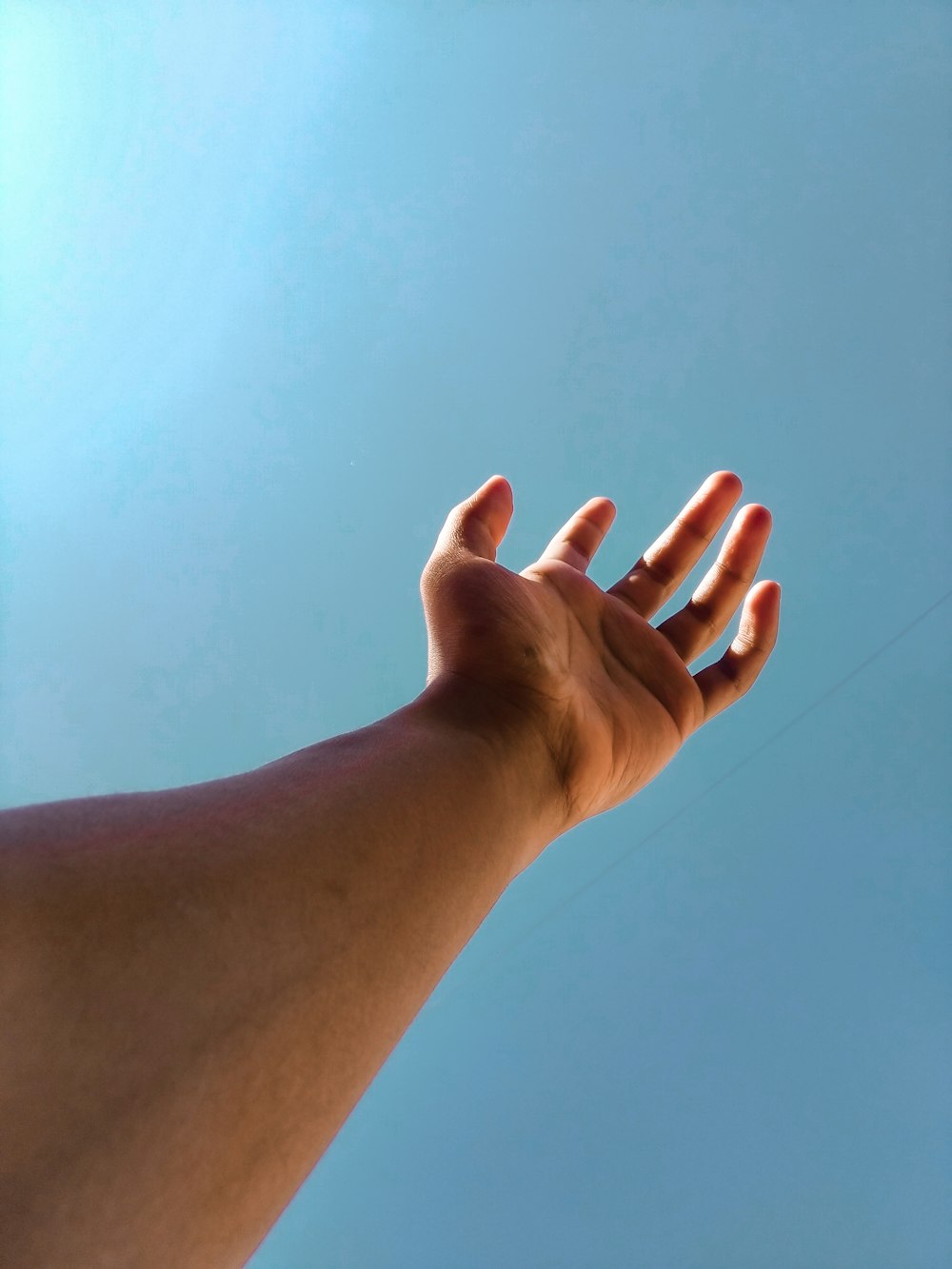 person raising right hand under blue sky during daytime