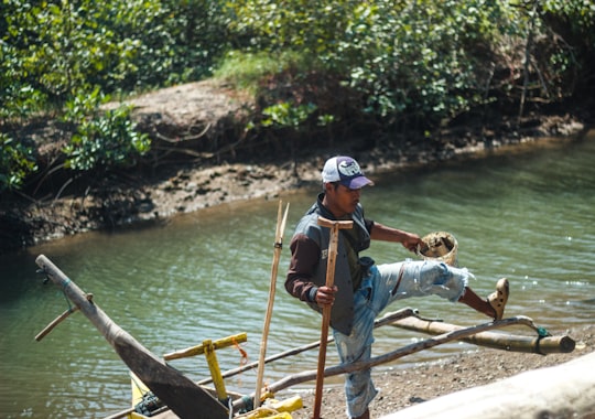 man in blue shirt and white helmet sitting on brown wooden boat during daytime in Gebang Indonesia