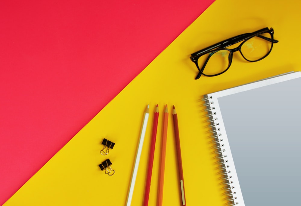 black framed eyeglasses beside white pencil on red table