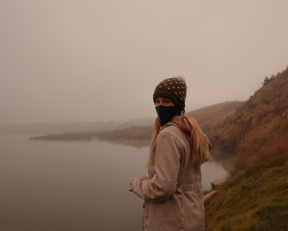 man in brown jacket standing on green grass field near body of water during daytime