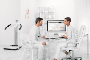 man in white dress shirt sitting on white chair in front of computer