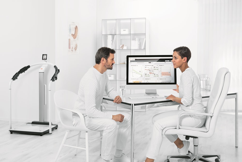 hombre en camisa de vestir blanca sentado en una silla blanca frente a la computadora