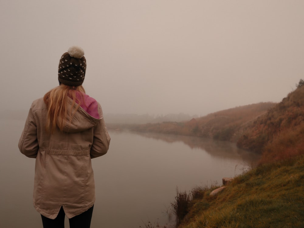 person in brown jacket standing on green grass field near lake during daytime