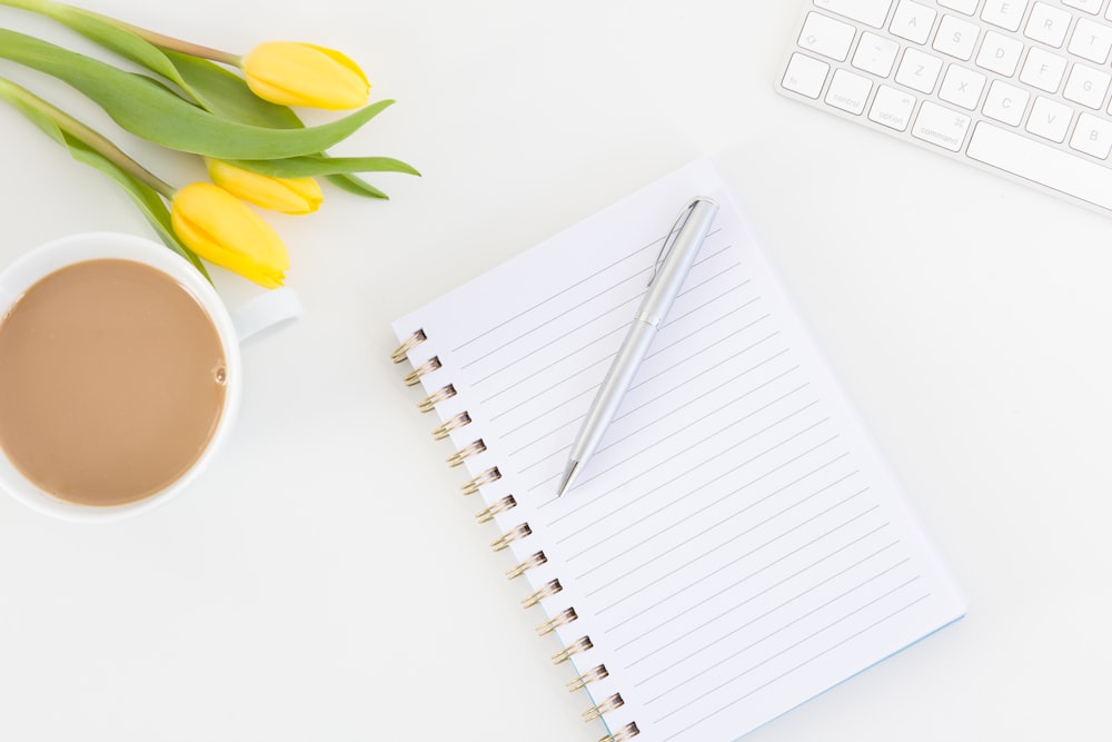 white notebook with yellow tulips beside white ceramic mug with coffee