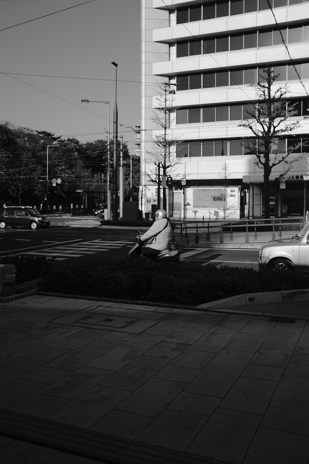 grayscale photo of man sitting on sidewalk near building