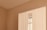 A section of a minimalist room featuring a white wardrobe against a light beige wall. The wardrobe includes a mirrored section that reflects part of a window with beige curtains. The clean lines and neutral tones create a calm, serene atmosphere.