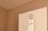 A section of a minimalist room featuring a white wardrobe against a light beige wall. The wardrobe includes a mirrored section that reflects part of a window with beige curtains. The clean lines and neutral tones create a calm, serene atmosphere.